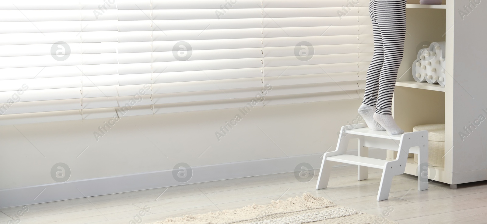 Photo of Little girl standing on step stool indoors, closeup. Space for text