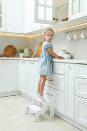 Photo of Little girl standing on step stool and reaching towards counter in kitchen