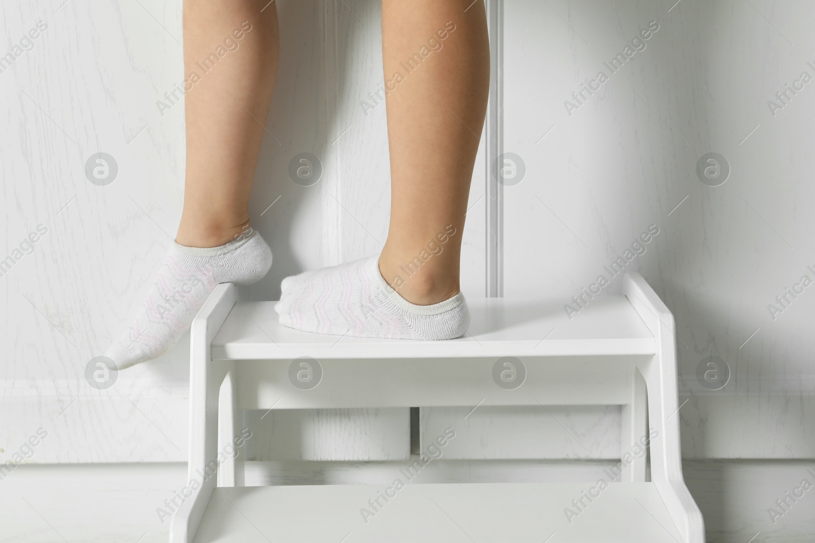 Photo of Little girl standing on step stool indoors, closeup