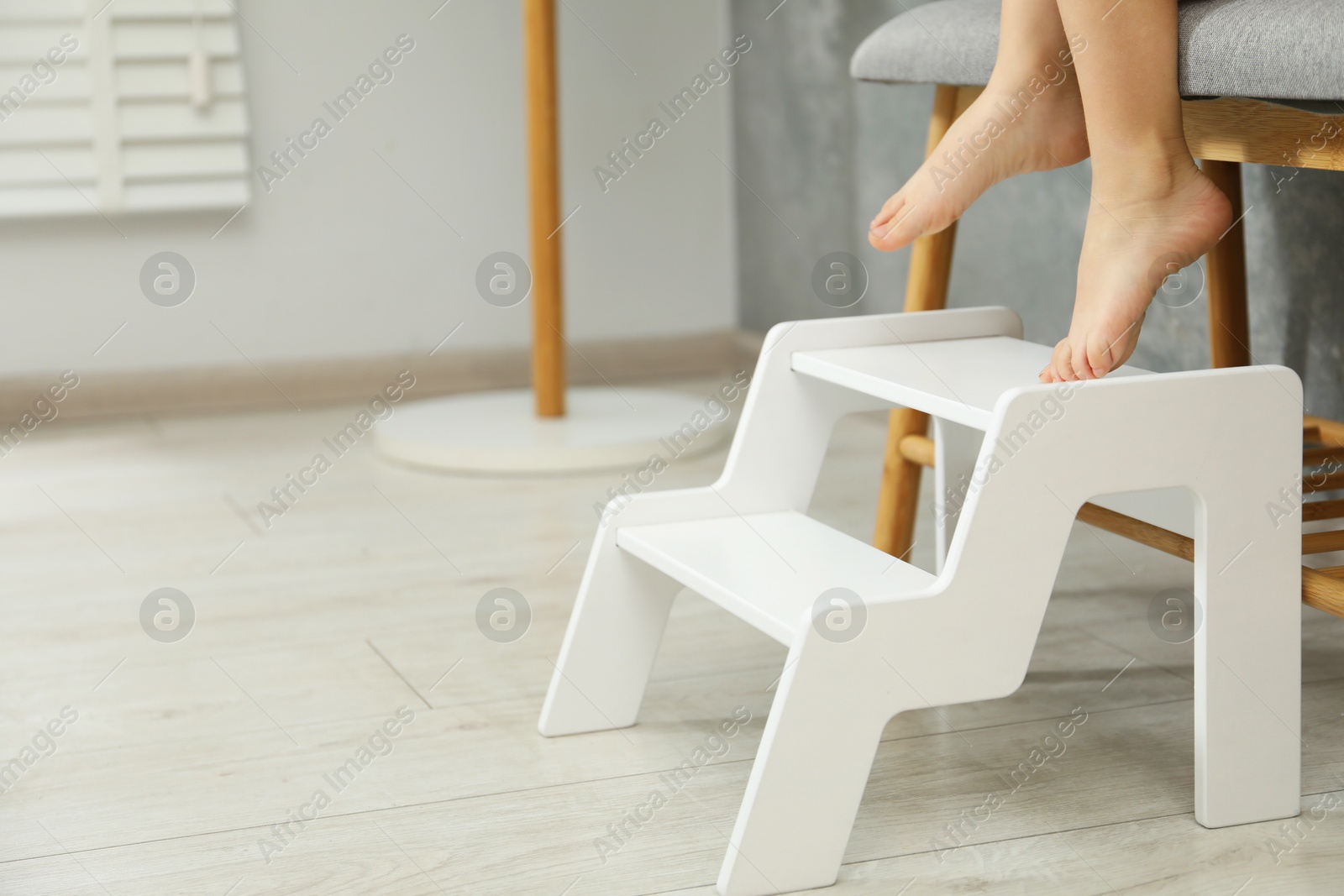 Photo of Little girl standing on step stool indoors, closeup. Space for text