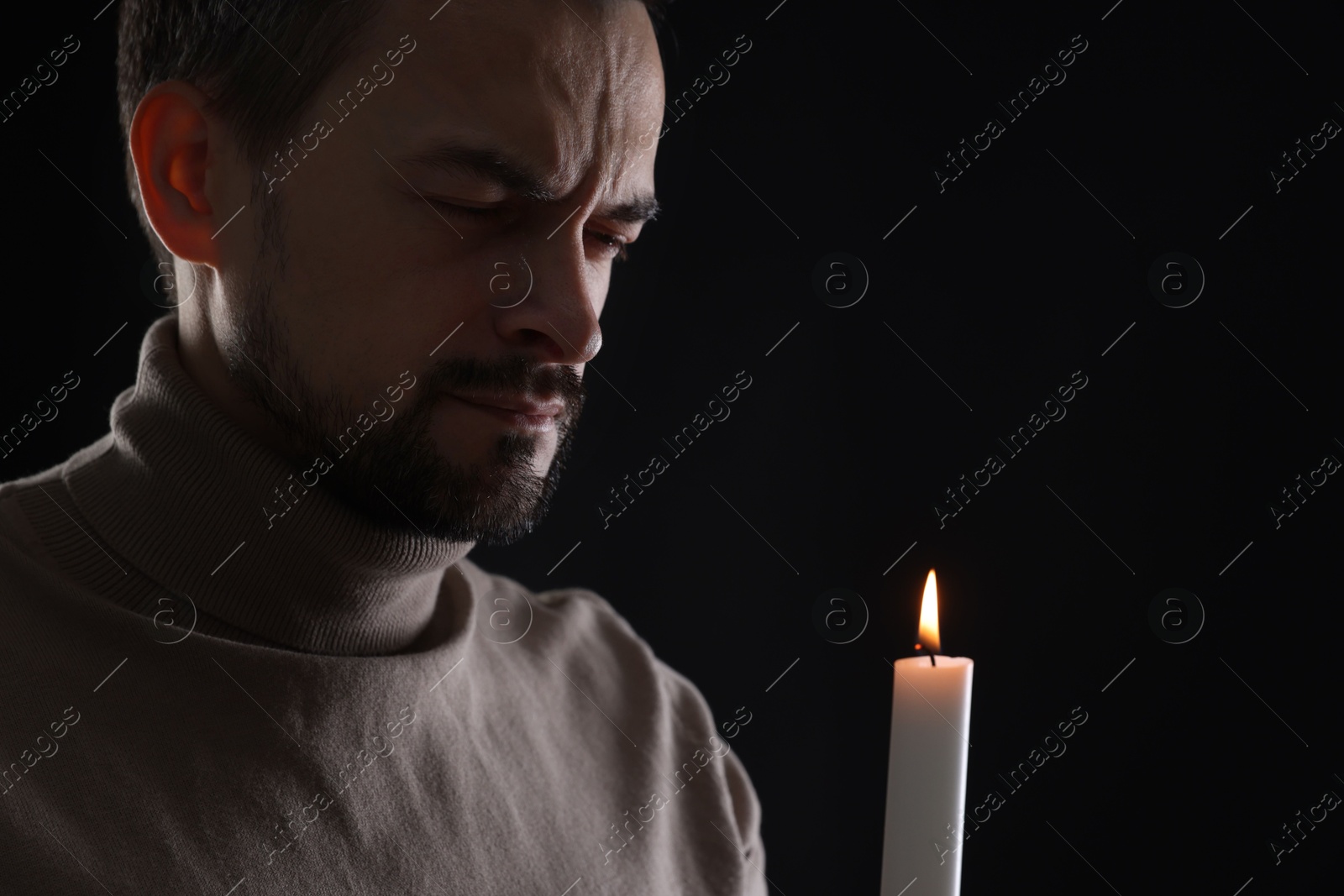 Photo of Sad man with burning candle crying on black background, space for text