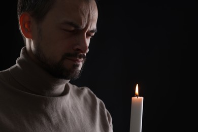 Photo of Sad man with burning candle crying on black background, space for text