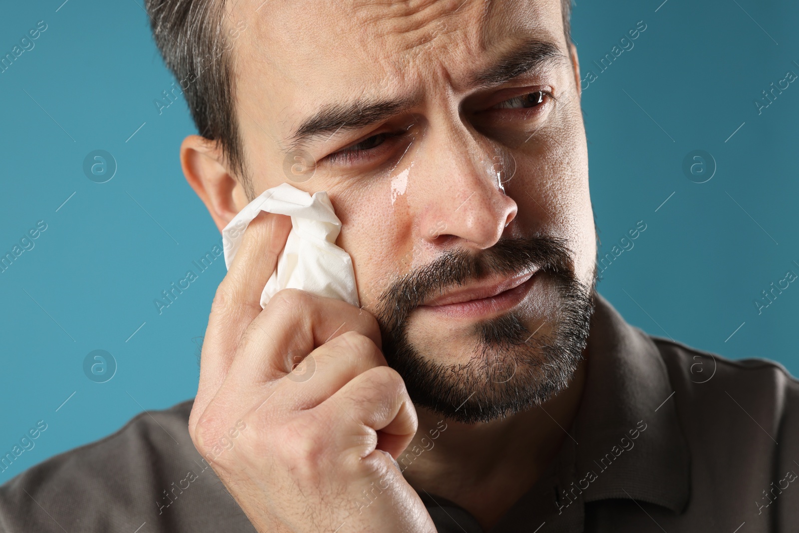 Photo of Sad man with paper tissue crying on light blue background