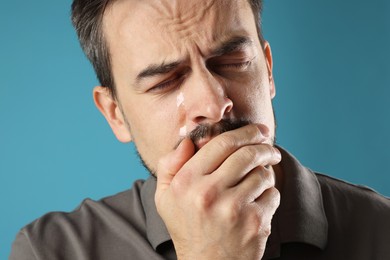 Photo of Sad man crying on light blue background, closeup