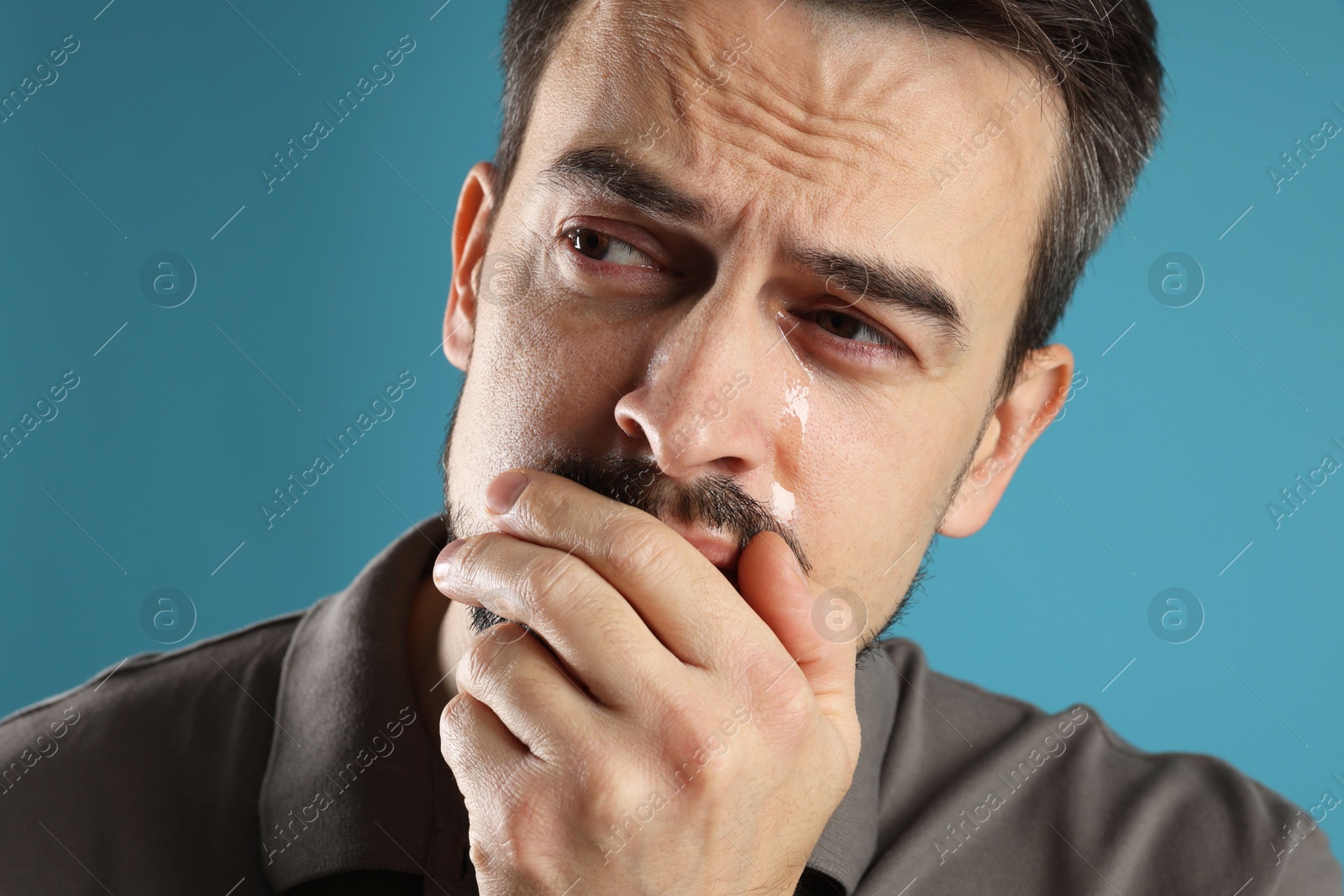 Photo of Sad man crying on light blue background, closeup