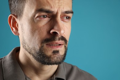 Photo of Sad man crying on light blue background, closeup