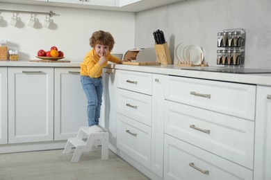 Photo of Little boy showing shush gesture while standing on step stool near countertop in kitchen