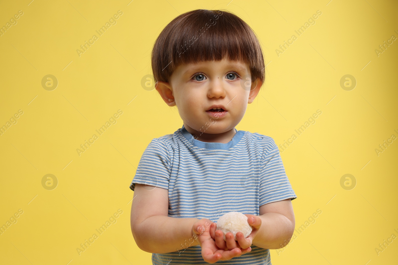 Photo of Cute little child with tasty mochi on yellow background