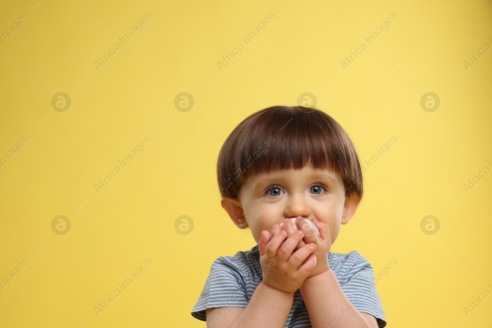 Photo of Cute little child eating tasty mochi on yellow background. Space for text