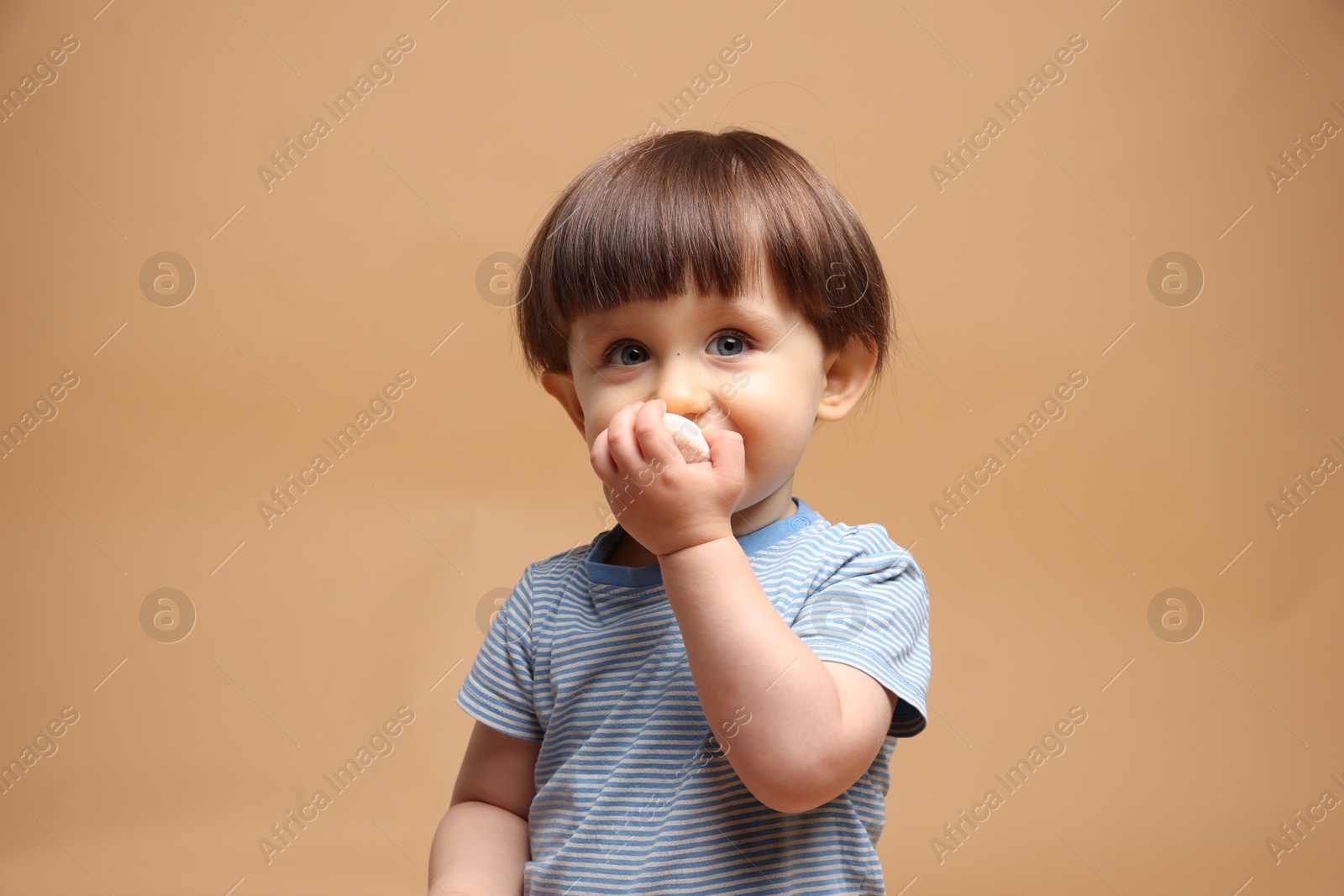 Photo of Cute little child eating tasty mochi on light brown background