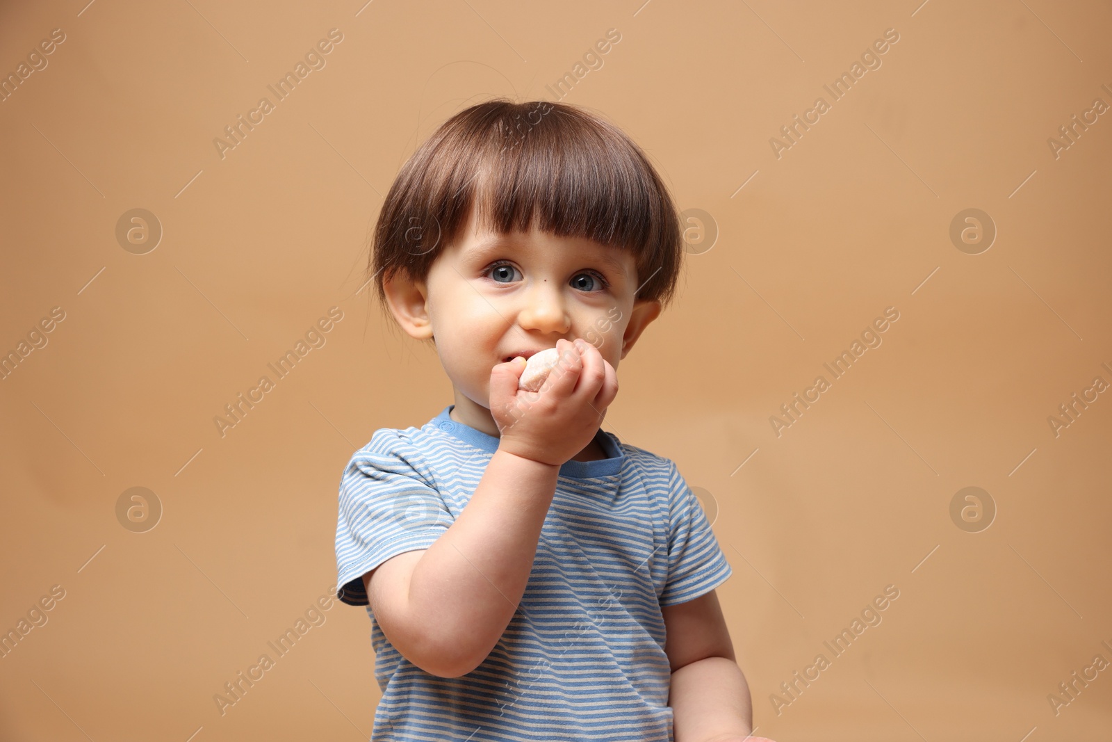 Photo of Cute little child eating tasty mochi on light brown background