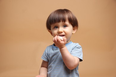 Photo of Cute little child eating tasty mochi on light brown background