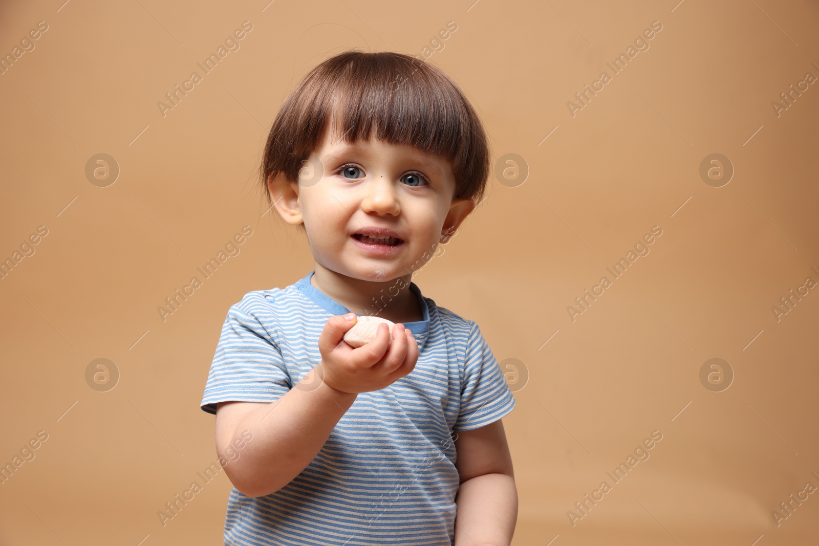 Photo of Cute little child with tasty mochi on light brown background