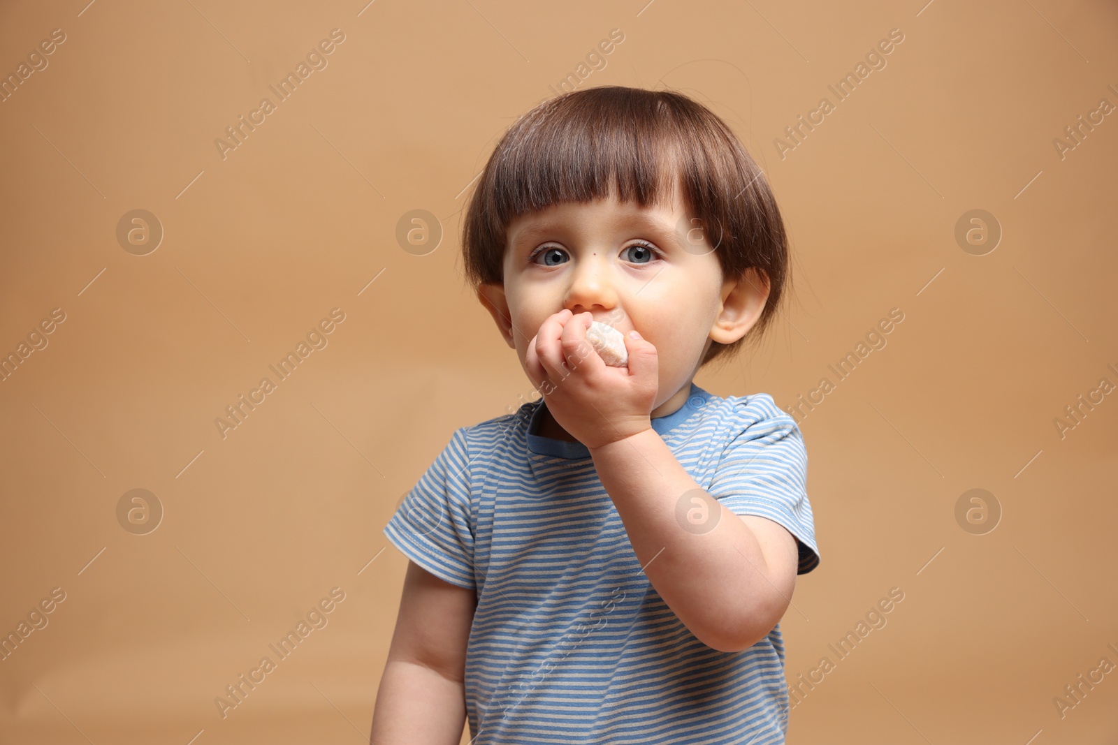 Photo of Cute little child eating tasty mochi on light brown background