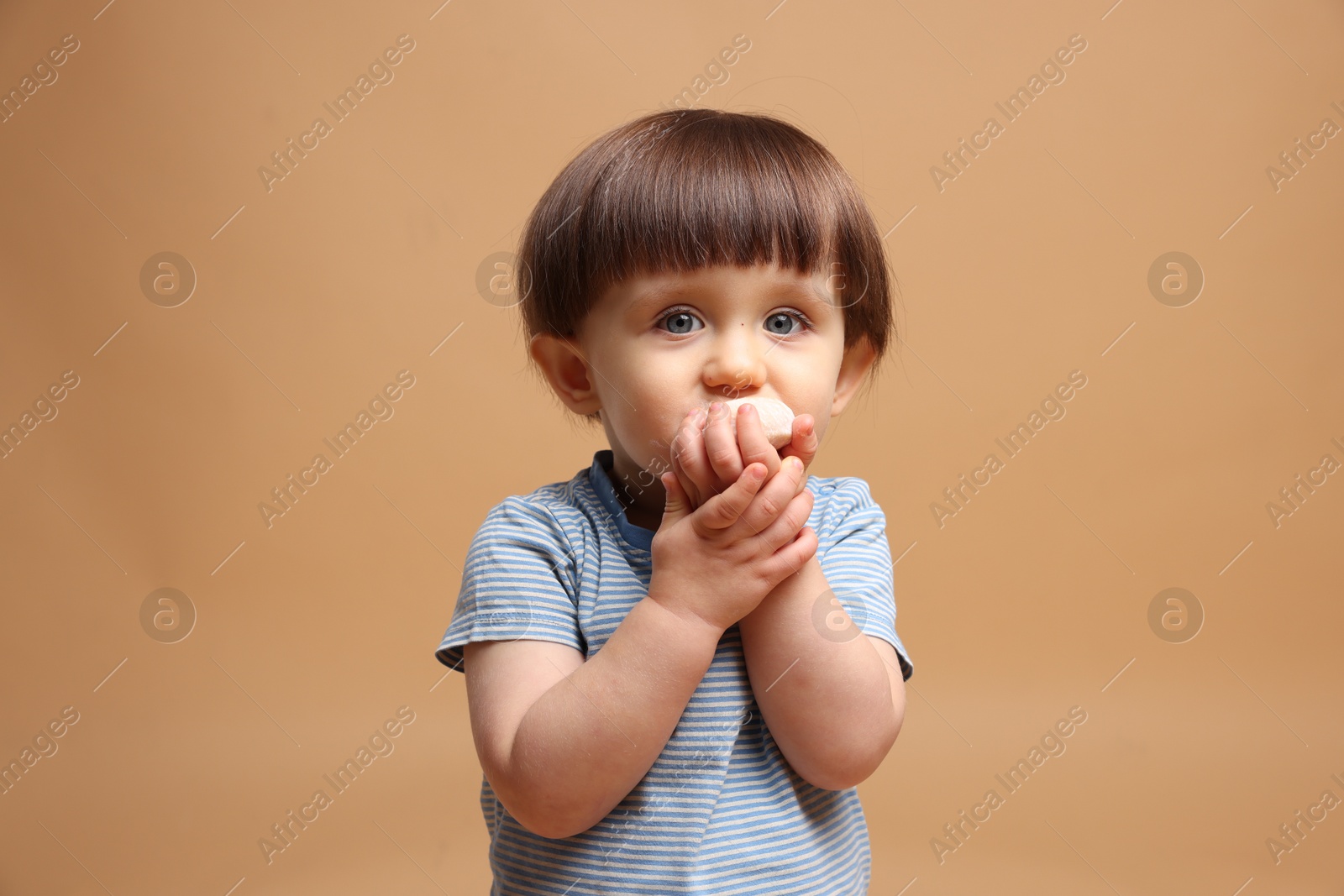 Photo of Cute little child eating tasty mochi on light brown background