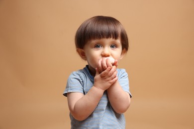 Photo of Cute little child eating tasty mochi on light brown background