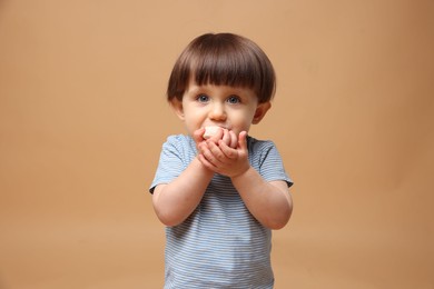 Photo of Cute little child eating tasty mochi on light brown background