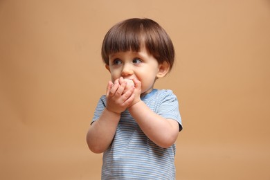 Photo of Cute little child eating tasty mochi on light brown background