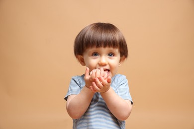 Photo of Cute little child eating tasty mochi on light brown background