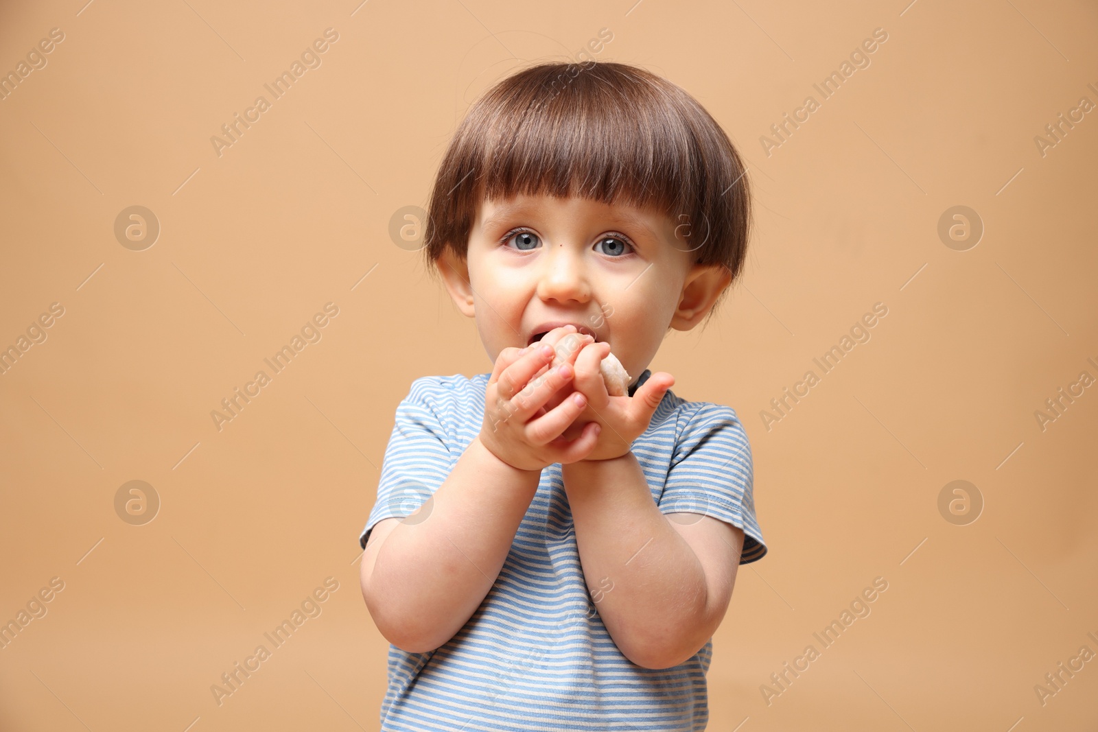 Photo of Cute little child eating tasty mochi on light brown background