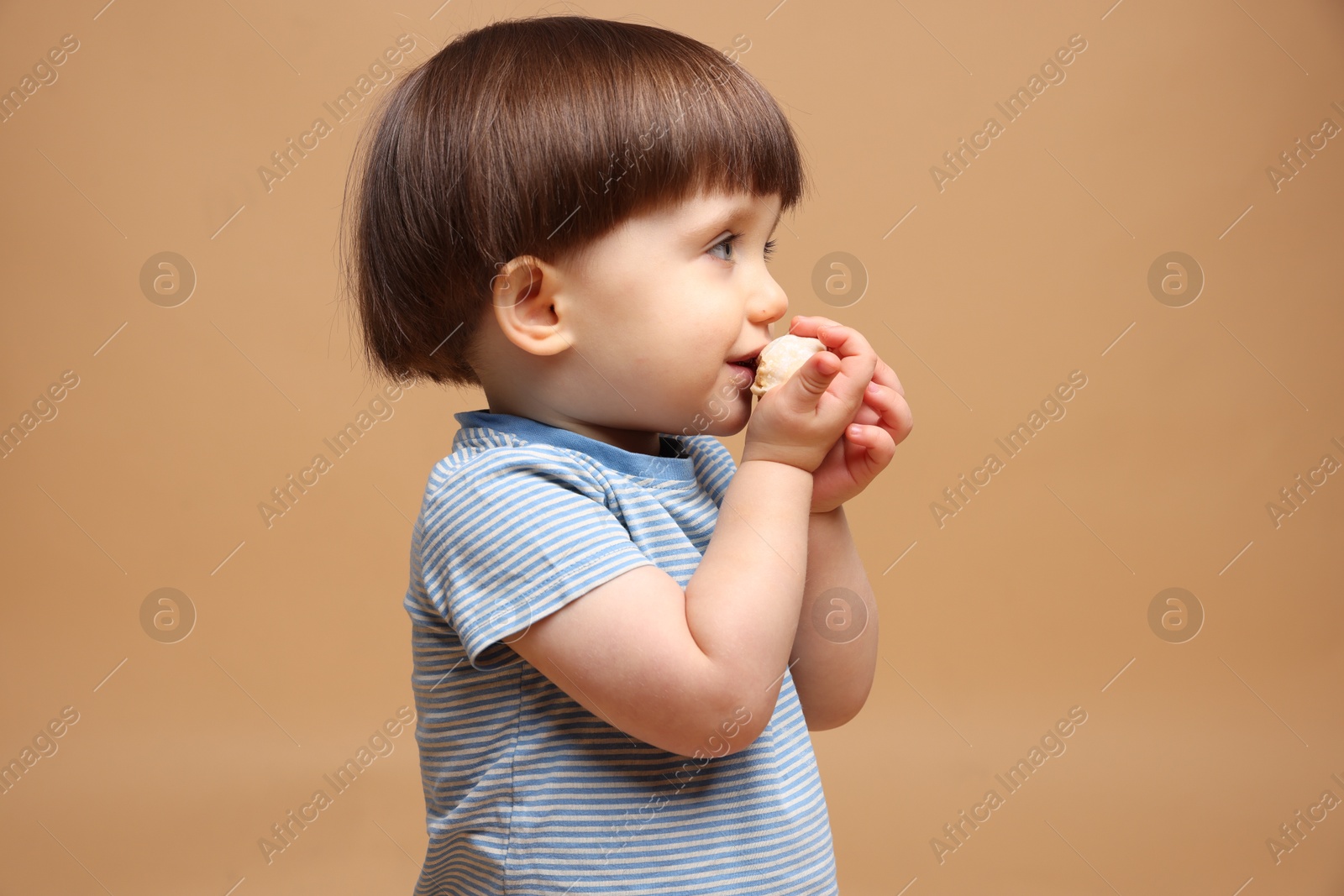 Photo of Cute little child eating tasty mochi on light brown background