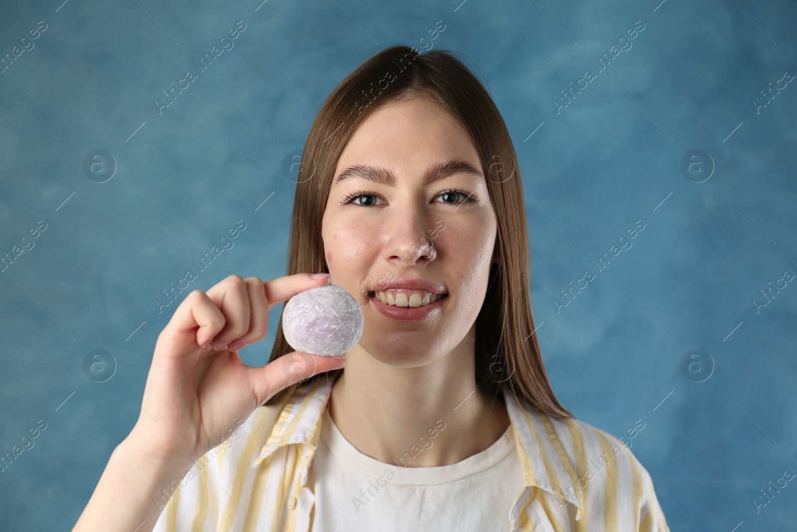 Photo of Smiling woman with tasty mochi on blurred blue background