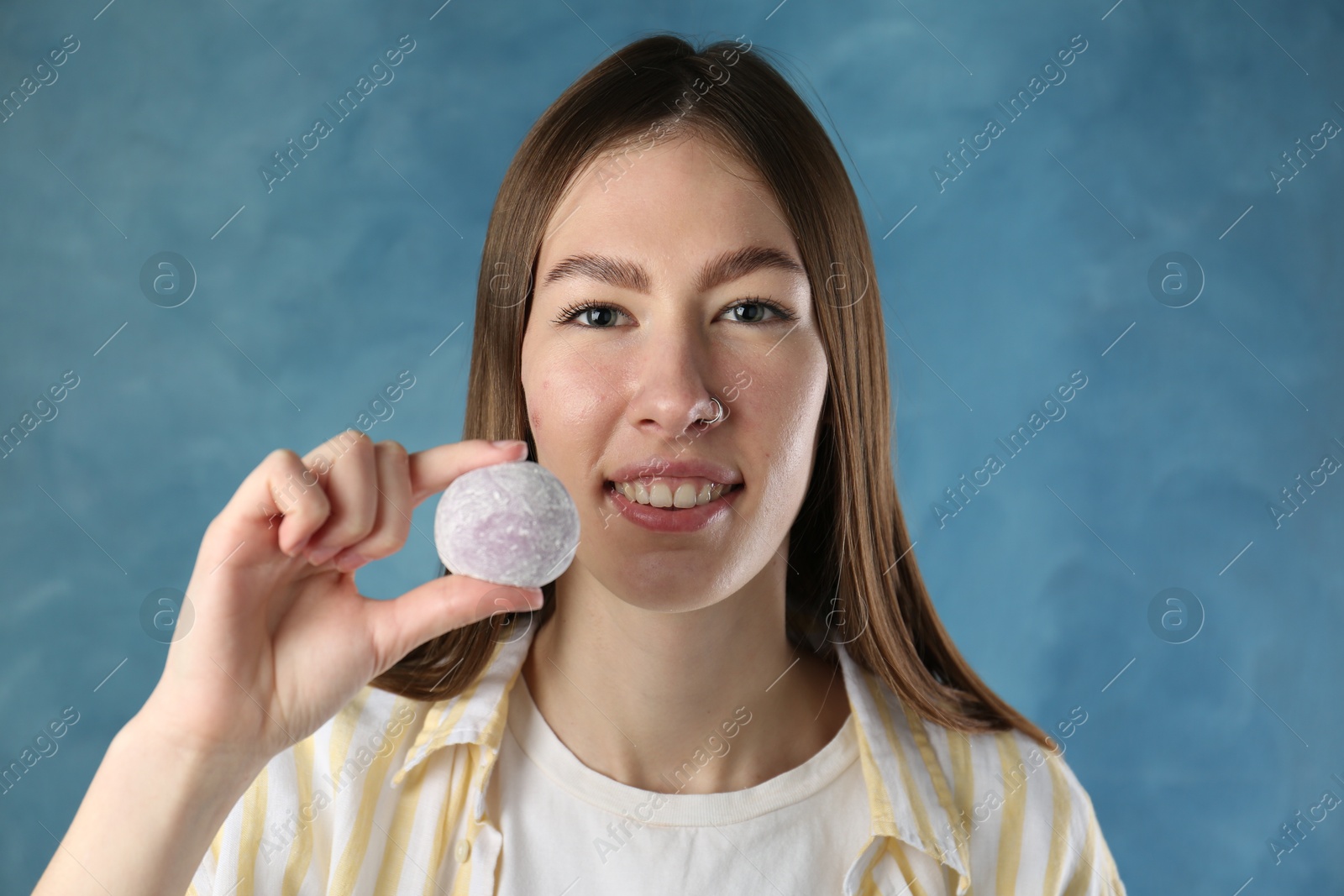 Photo of Smiling woman with tasty mochi on blurred blue background