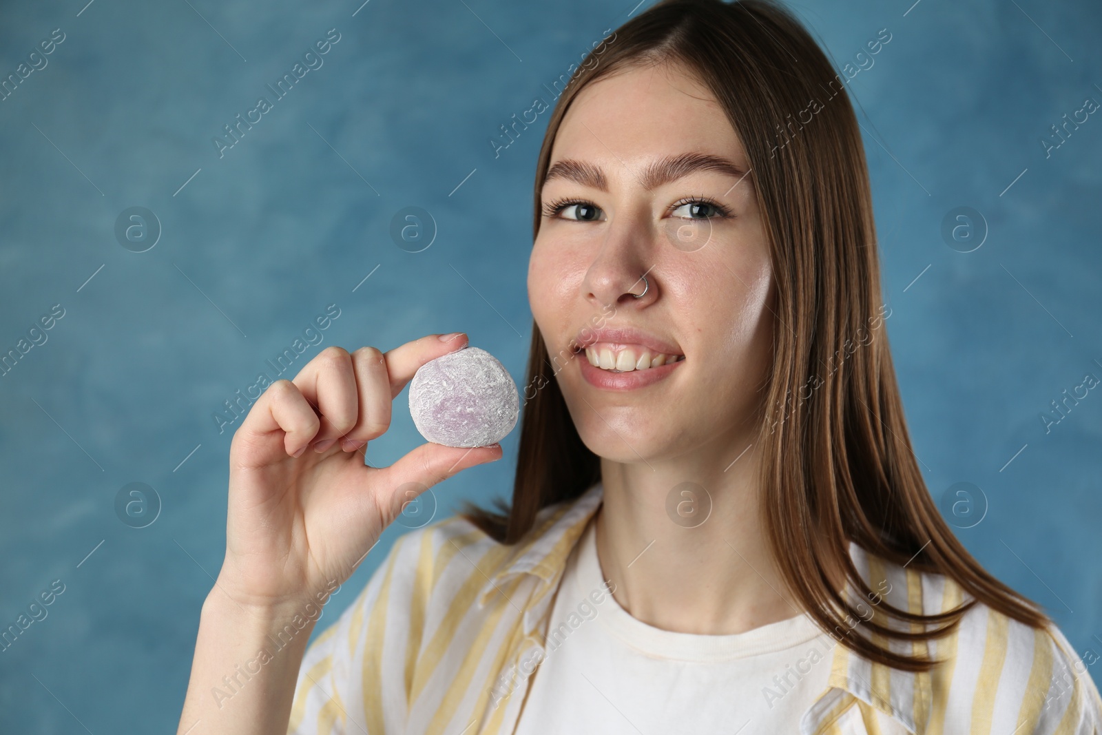 Photo of Smiling woman with tasty mochi on blurred blue background. Space for text