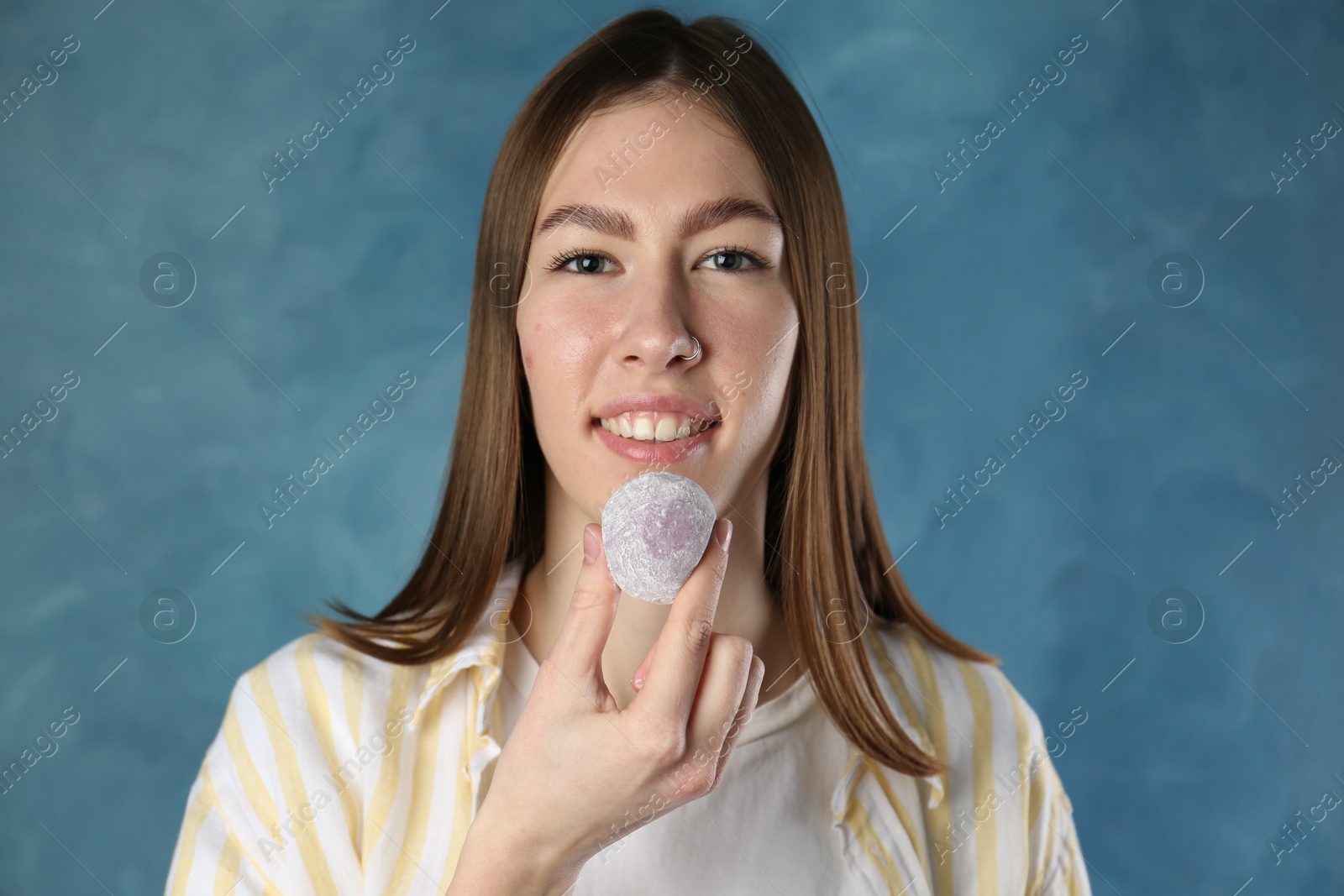 Photo of Smiling woman with tasty mochi on blurred blue background