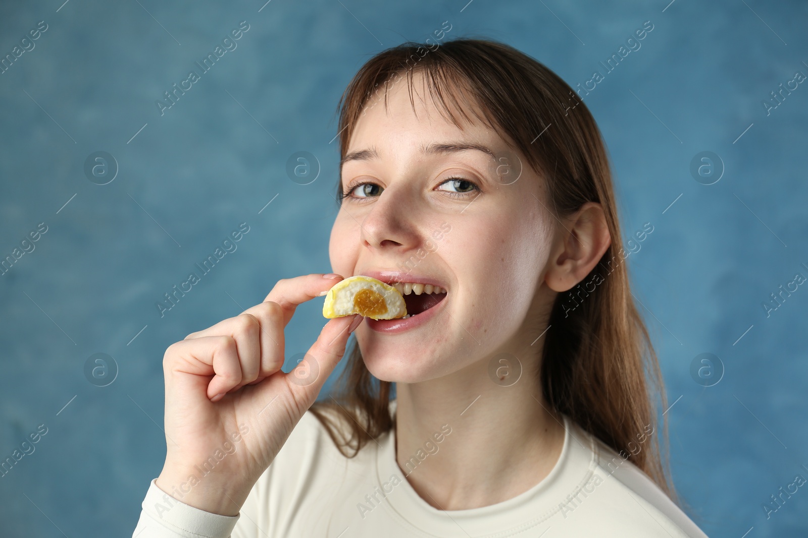 Photo of Beautiful woman eating tasty mochi on blurred blue background