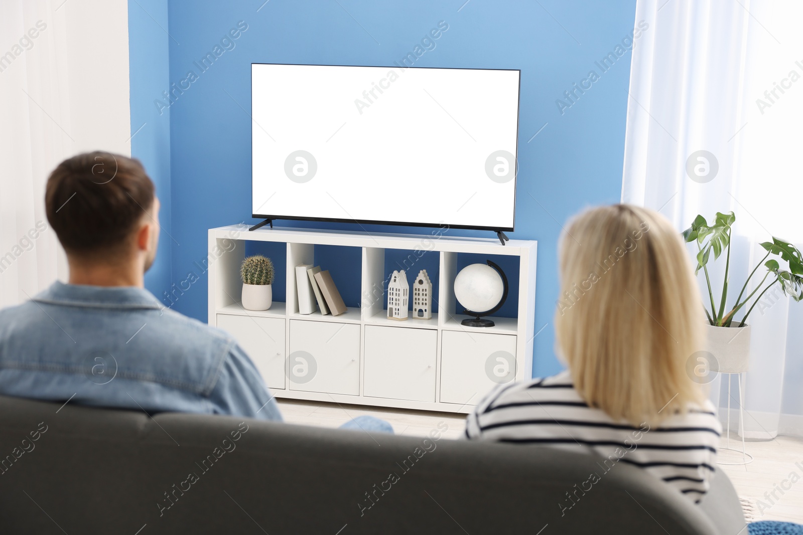 Photo of Lovely couple watching tv on couch at home, back view