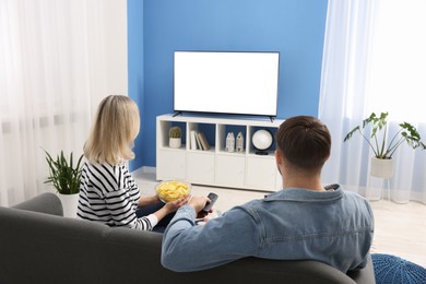 Photo of Lovely couple with chips watching tv on couch at home, back view