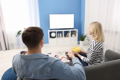 Photo of Lovely couple with chips watching tv on couch at home, back view