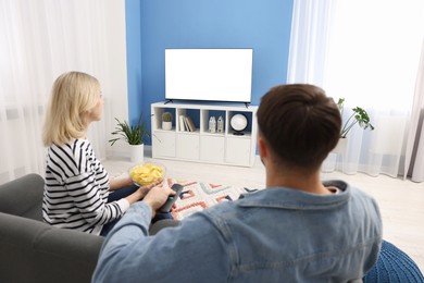 Photo of Lovely couple with chips watching tv on couch at home, back view