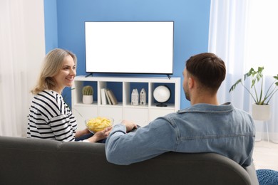 Photo of Lovely couple with chips watching tv on couch at home