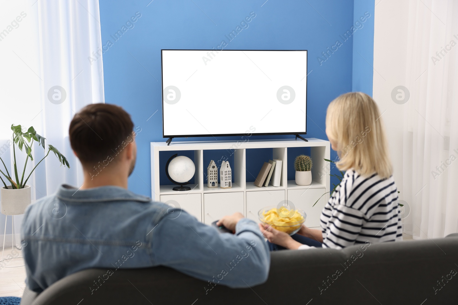 Photo of Lovely couple with chips watching tv on couch at home, back view