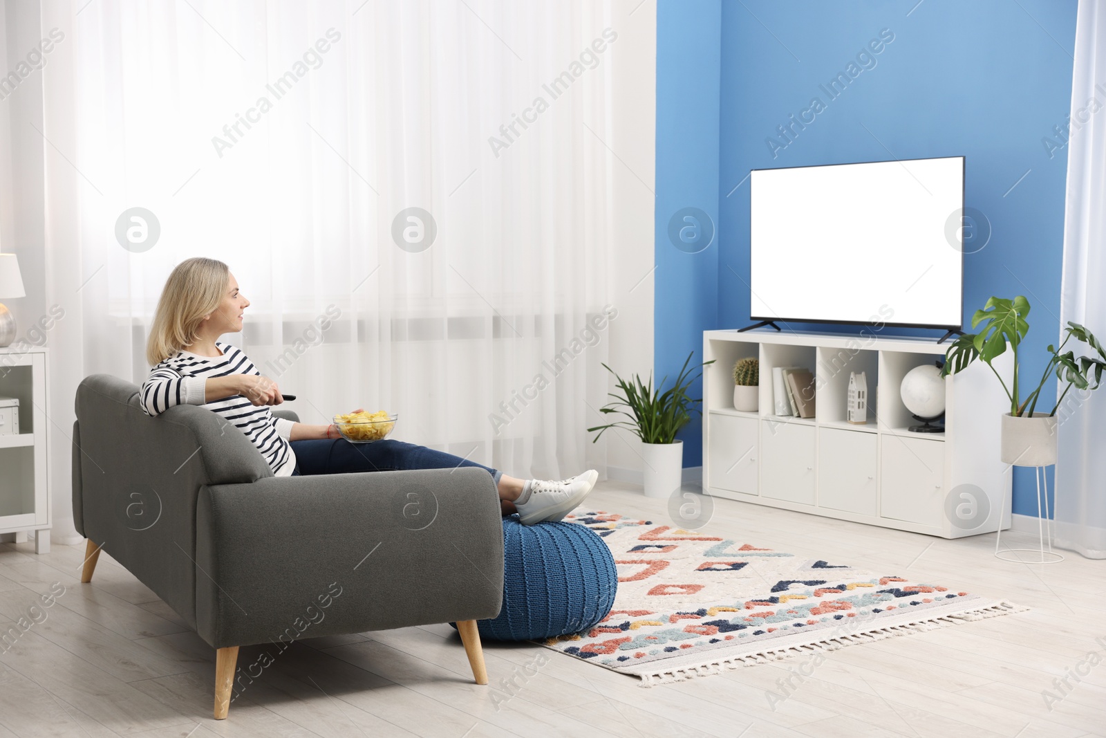 Photo of Woman with chips watching tv on couch at home