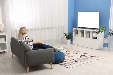 Woman with chips watching tv on couch at home