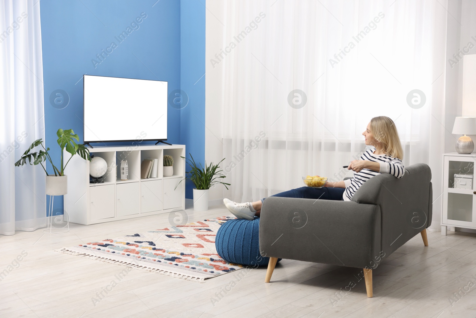 Photo of Woman with chips watching tv on couch at home