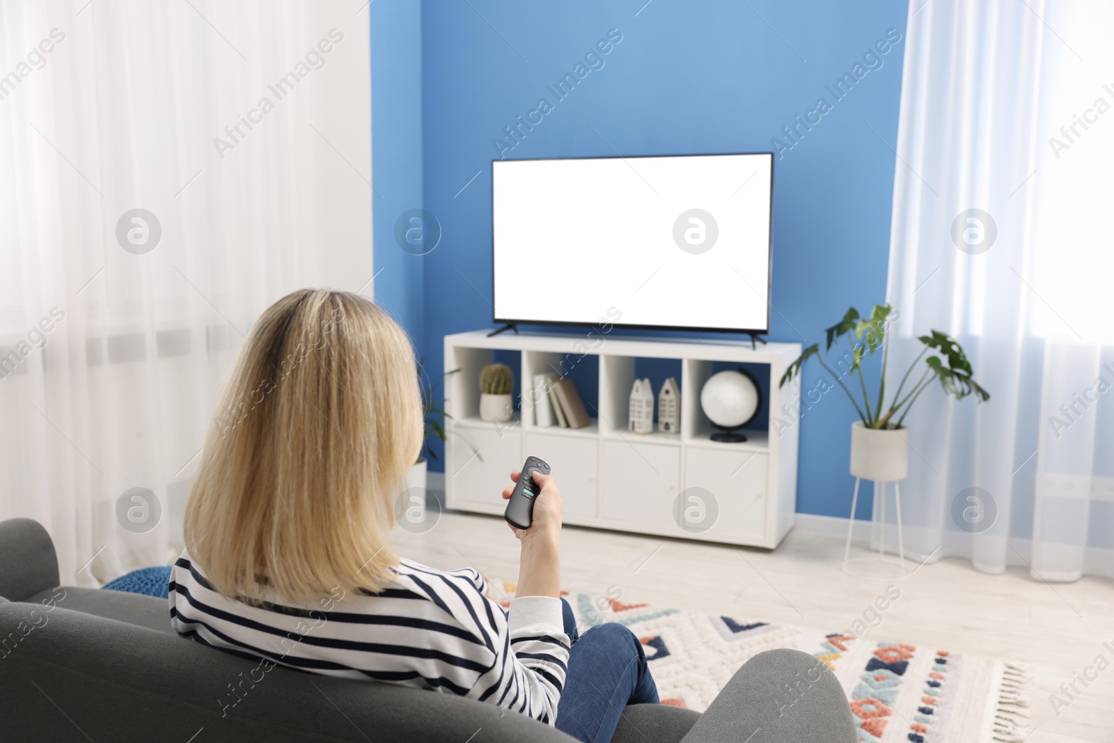 Photo of Woman watching tv on couch at home, back view