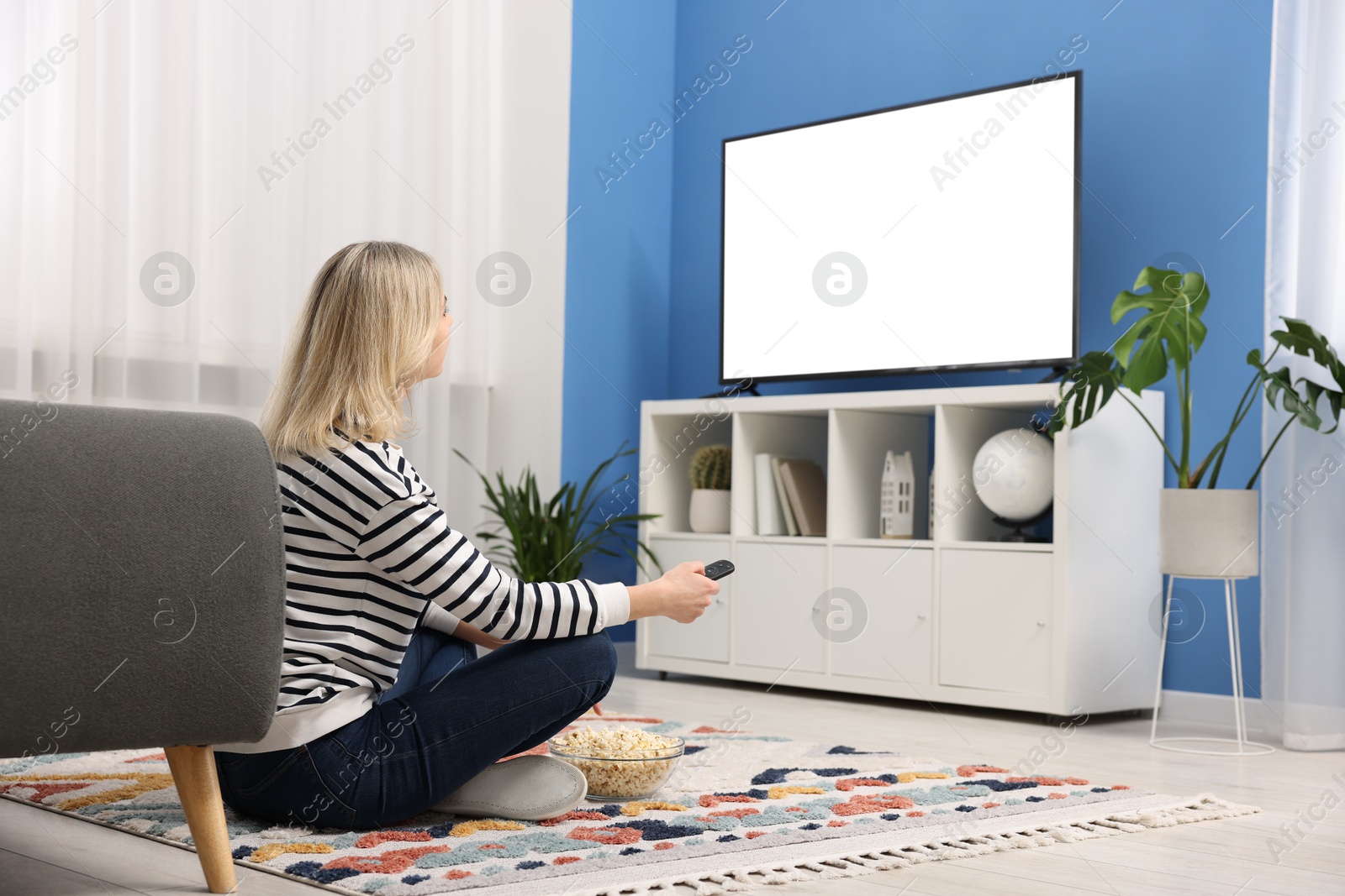 Photo of Woman with popcorn watching tv on floor at home