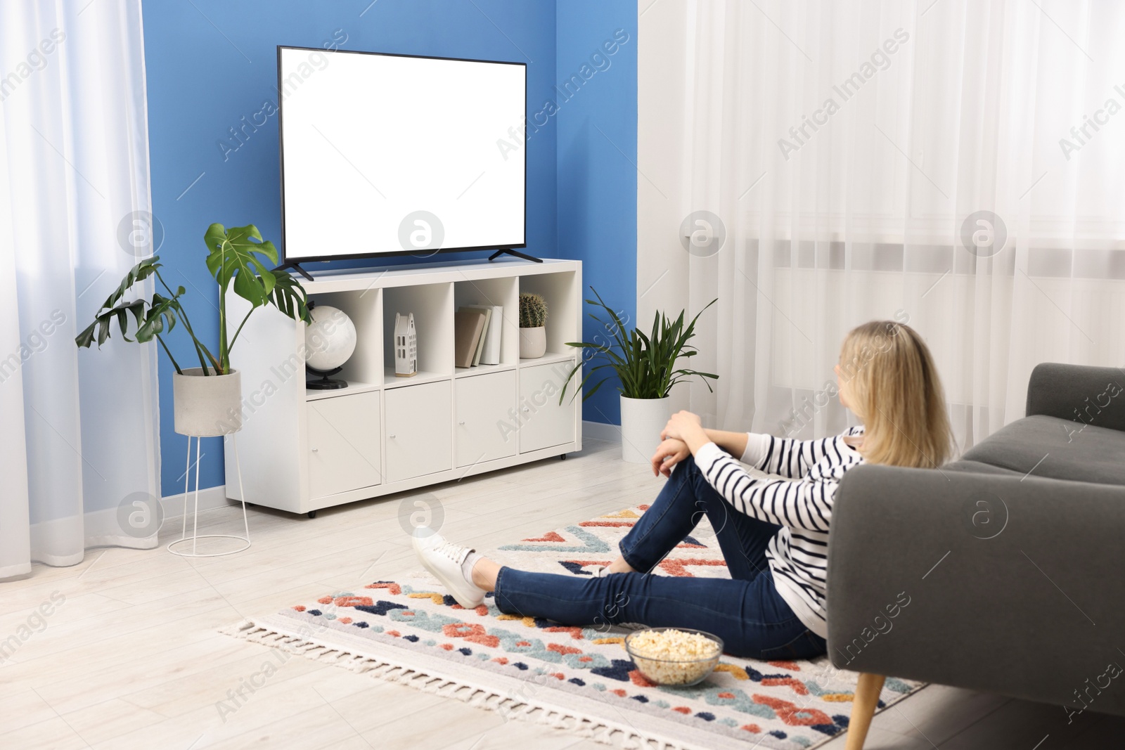 Photo of Woman with popcorn watching tv on floor at home