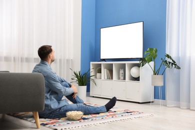 Photo of Man with popcorn watching tv on floor at home