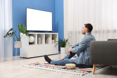 Photo of Man with popcorn watching tv on floor at home