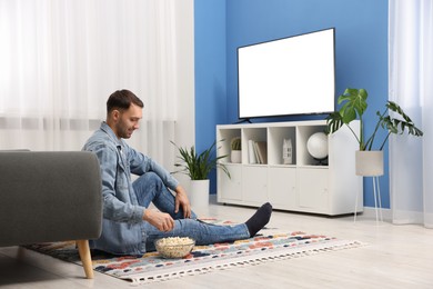 Photo of Man with popcorn watching tv on floor at home