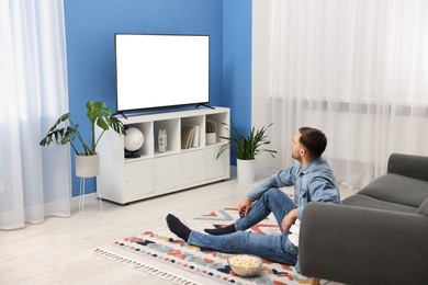 Man with popcorn watching tv on floor at home