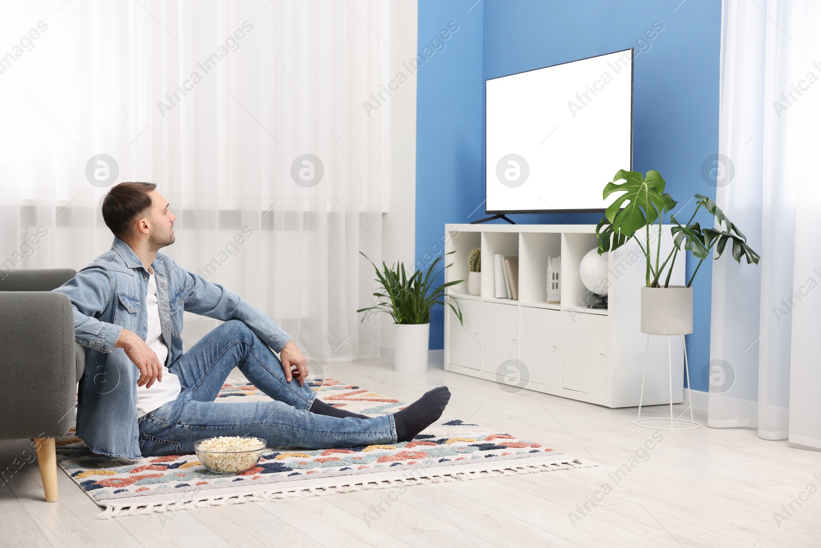 Photo of Man with popcorn watching tv on floor at home