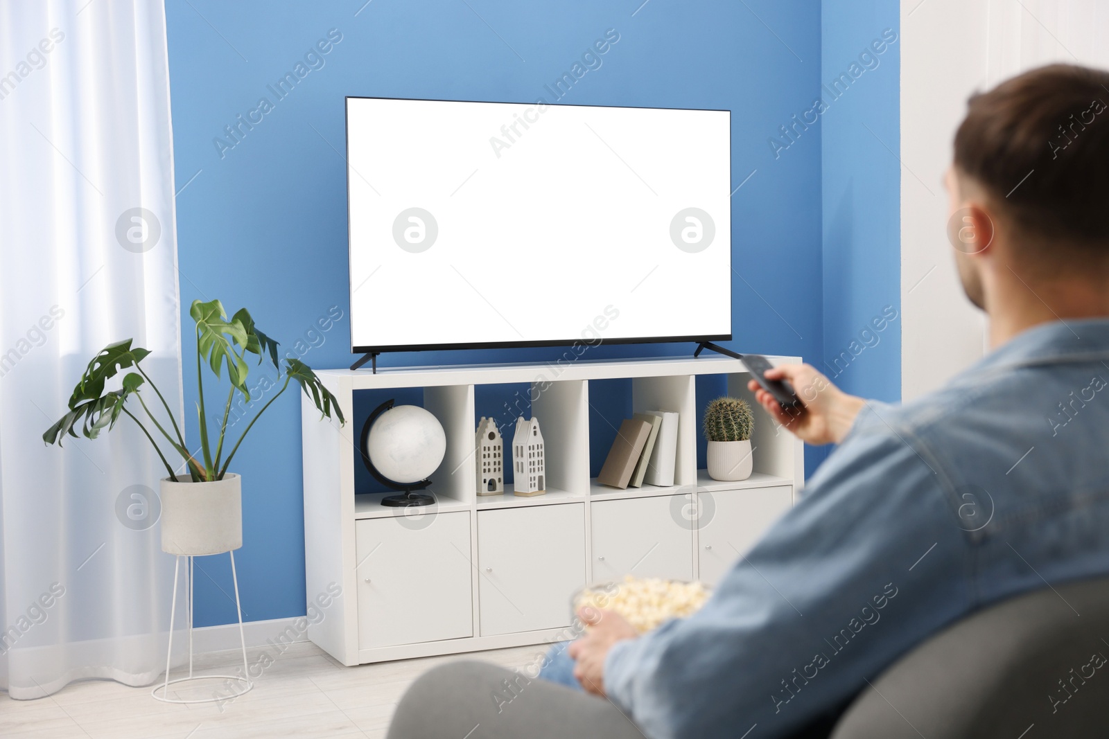 Photo of Man with popcorn watching tv on couch at home, back view