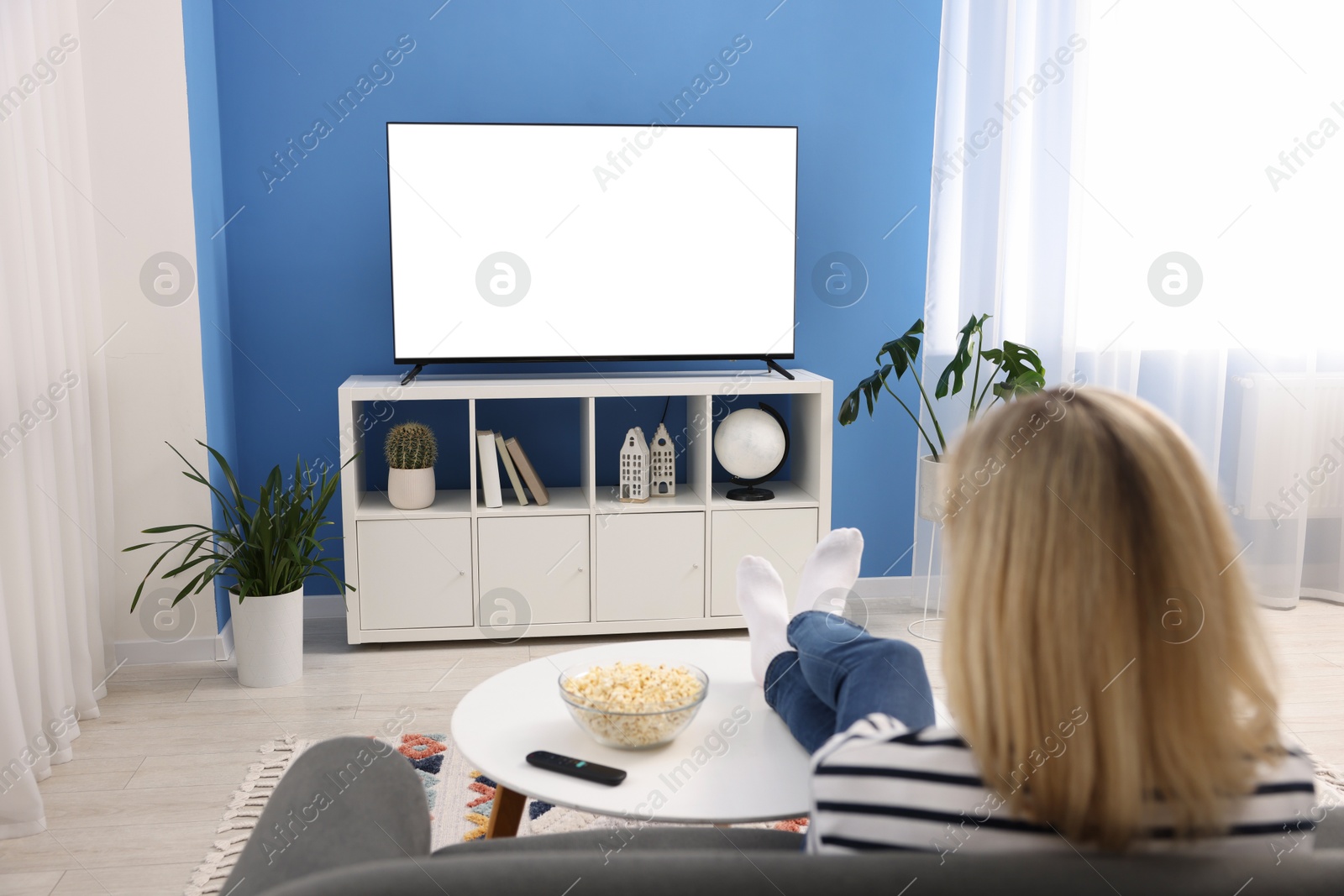 Photo of Woman watching tv on couch at home, back view