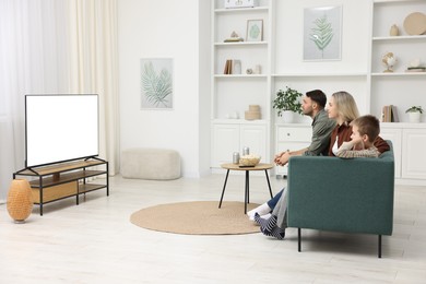 Photo of Happy family with snacks and drinks watching tv together at home